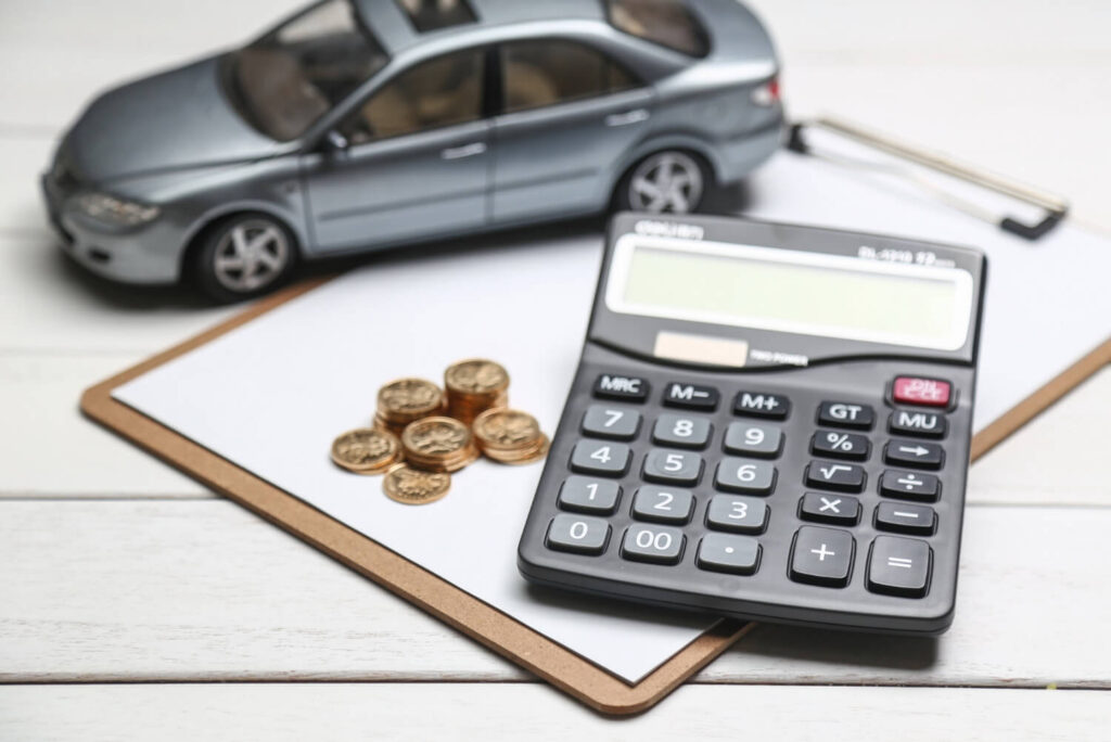 Calculadora, moedas e miniatura de carro representam o cálculo das despesas com o carro.