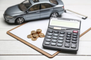 Calculadora, moedas e miniatura de carro representam o cálculo das despesas com o carro.