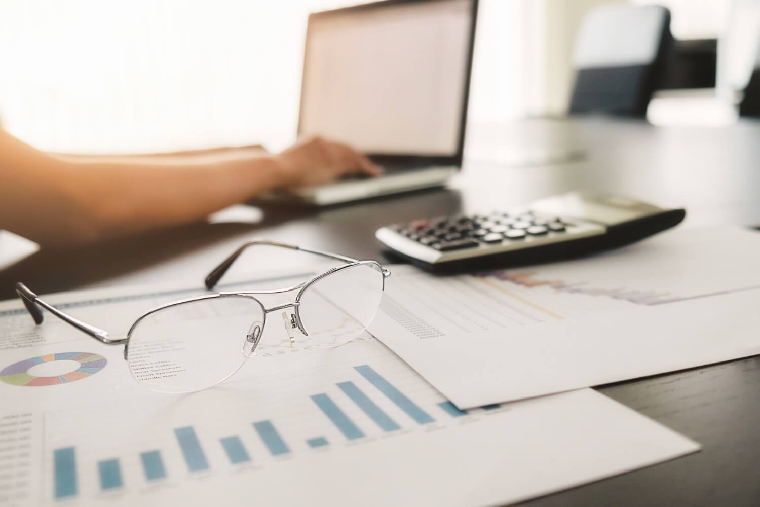 Mulher faz análise de crédito com apoio de gráficos, notebook e calculadora.
